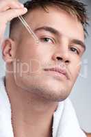 Beauty is unisex. Closeup shot of a young handsome man applying serum to his face against a grey background.