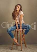 Shes just what you need on a cloudy day. Studio shot of a beautiful young woman sitting on a stool against a plain background.
