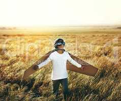 Kids love to let their imagination fly. Shot of a young boy pretending to fly with a pair of cardboard wings in an open field.