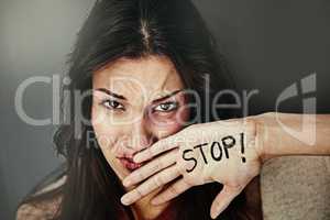 Its about time we put a stop to domestic abuse. Portrait of a beaten and bruised young woman with the word STOP written on her hand.