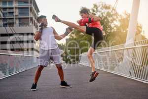 Working on her kicks. Shot of a young couple going through some kickboxing routines outdoors on a bridge.