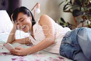 I would listen to this song endlessly. Shot of a young woman lying on her bed listening to music on her smartphone at home.