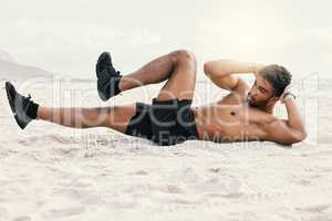 Im working on that six-pack. Shot of a sporty young man doing crunches while at the beach for a workout.