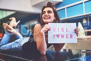 She has a whole lot of girl power. Shot of an attractive young woman lying on top of a counter while holding a sign saying girl power inside of a laundry room during the day.