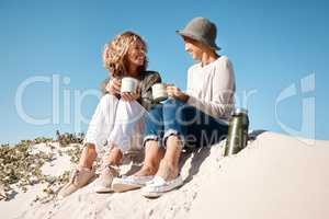 Making the beach their own personal cafe. Full length shot of two attractive mature women enjoying some coffee while sitting on the beach.