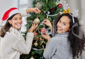 Time to decorate the tree. Shot of two young women decorating the Christmas tree at home.