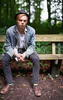 Getting away from it all. Portrait of a handsome and stylish young man sitting on a bench in a forest.