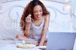 This is my favourite comedian. Shot of a woman laughing while lying on her bed with her laptop and a bowl of popcorn.