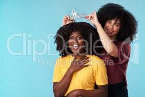 Empowered women, empower women. Studio shot of a young woman putting a crown on her friend against a blue background.
