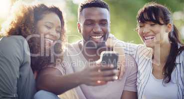 Were starting to trend again guys. Shot of a cheerful group of friends using a cellphone together while relaxing outdoors.