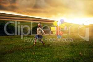 Frolicking through the fields. Shot of a playful little girl running through a field while holding a bunch of balloons.