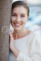 There are so many beautiful reasons to be happy. Portrait of a smiling young woman leaning against a tree outside.