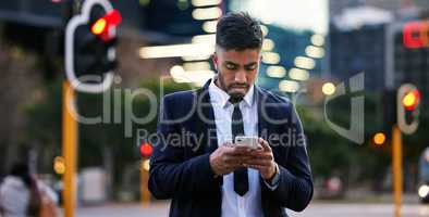 You finally received my text. Shot of a handsome young businessman walking around town using his smartphone.