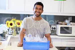 Not all heroes wear capes. Shot of a young man getting ready to recycle some bottles at home.