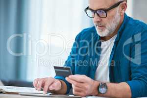 I wonder when my package will arrive. Shot of a senior businessman using his digital tablet to make online card payments.