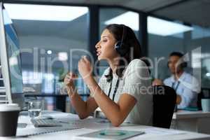 Hang in there, help is on the way. Shot of a young woman using a headset and computer in a modern office.