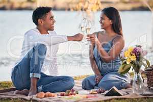 Heres to over everlasting love. Shot of a young couple making a toast while on a picnic at a lakeside.