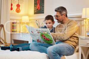 Learning about the history of these fascinating creatures. Shot of a father and son reading a book about dinosaurs together in a bedroom at home.