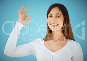 Alright with me. Studio shot of a young woman showing an OK against a blue background.
