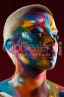 Its all in the shades. Studio shot of a young woman posing with multi-coloured paint on her face.