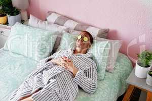 Face mask and chill. High angle shot of an attractive young woman lying on her bed with a mud mask and cucumber slices on her face at home.