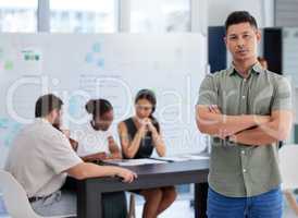 Leading his team with utmost dedication. Portrait of a confident young businessman standing in an office with his colleagues in the background.