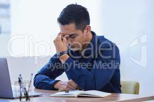 Overwhelmed with too much to do. Shot of a young businessman looking stressed out while working in an office.