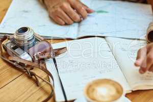 His travel journal keeps him on track. Shot of an unidentifiable tourist looking at maps and travel journals while enjoying coffee at a cafe.