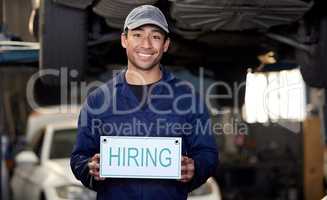 Have you got the skills required. Cropped portrait of a handsome young male mechanic holding a hiring sign while standing in his workshop.