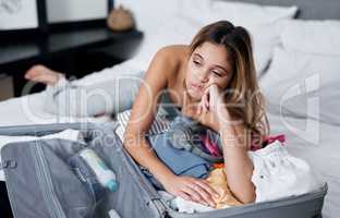 Covid-19 ruined everyones traveling plans. Shot of a woman looking displeased while lying on her bed with a packed suitcase.