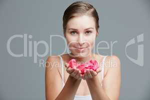 Beauty inspired by the softness of petals. Studio portrait of an attractive young woman holding a handful of pink petals against a gray background.