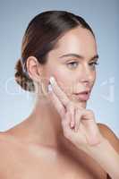 Keeping her skin nice and healthy. Studio shot of an attractive young woman moisturizing her face against a grey background.