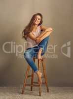 Just be happy with yourself. Studio shot of a beautiful young woman sitting on a stool against a plain background.