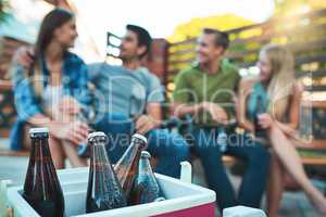 They dont call it a chill out session for nothing. Shot of bottled beers chilling in a cooler box with a group of friends hanging out in the background.