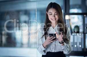 She hustles at all hours. Shot of a young businesswoman using a cellphone in an office at night.