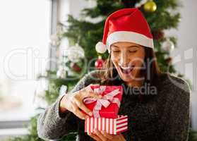 Christmas is the day that holds all time together. Shot of a young woman opening presents during Christmas at home.