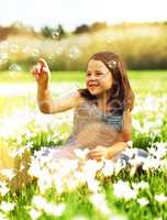Having a little bubble fun in the sun. Shot of an adorable little girl playing with bubbles while sitting in a field of wildflowers outside.