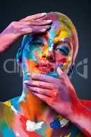 Color is all about expression. Studio shot of a young woman posing with multi-coloured paint on her face.