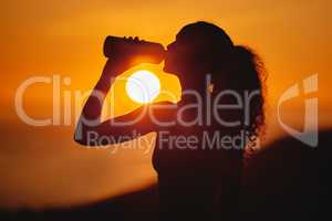 Stay hydrated. Cropped shot of an unrecognizable and athletic young woman drinking water while exercising outside at sunset.