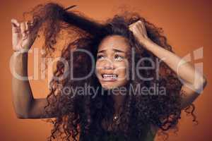 I thought going natural would be less of a struggle. Shot of a woman crying while combing our her curls against an orange background.