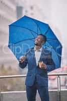 The weathers looking great today. Shot of a young businessman holding an umbrella in the rain against a city background.