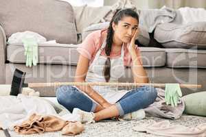 Can these chores just disappear. Shot of a young woman sitting looking overwhelmed while sitting in a messy living room at home.