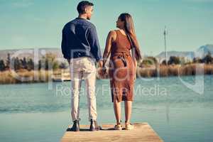 You are the whole of my heart. Rearview shot of a young couple holding hands while standing together on a pier at a lakeside.
