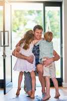 Dads always greeted by tons of love. Shot of a father embracing his two little children as he enters the house.