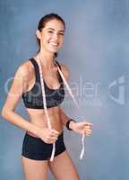 Im getting in the best shape of my life. Studio portrait of a sporty young woman posing with a tape measure against a grey background.