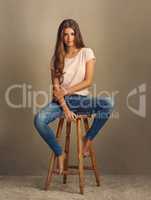 do you know how perfect you are. Studio shot of a beautiful young woman sitting on a stool against a plain background.