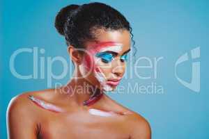 Face paint bring forth her true nature. Studio shot of a beautiful young woman covered in face paint posing against a blue background.