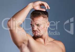 I smell really bad. Studio shot of a young man smelling his armpit against a grey background.
