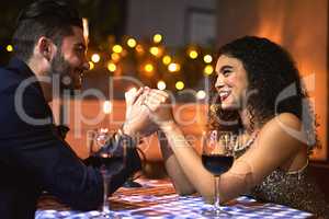 We will stay together forever. Shot of a cheerful young couple holding hands while looking into each others eyes over a candle lit dinner date at night.
