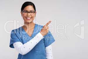 Doctors eliminate the nos on their vacancy signs to exist. Portrait of a young doctor wearing glasses and scrubs, pointing to her left against a white background.